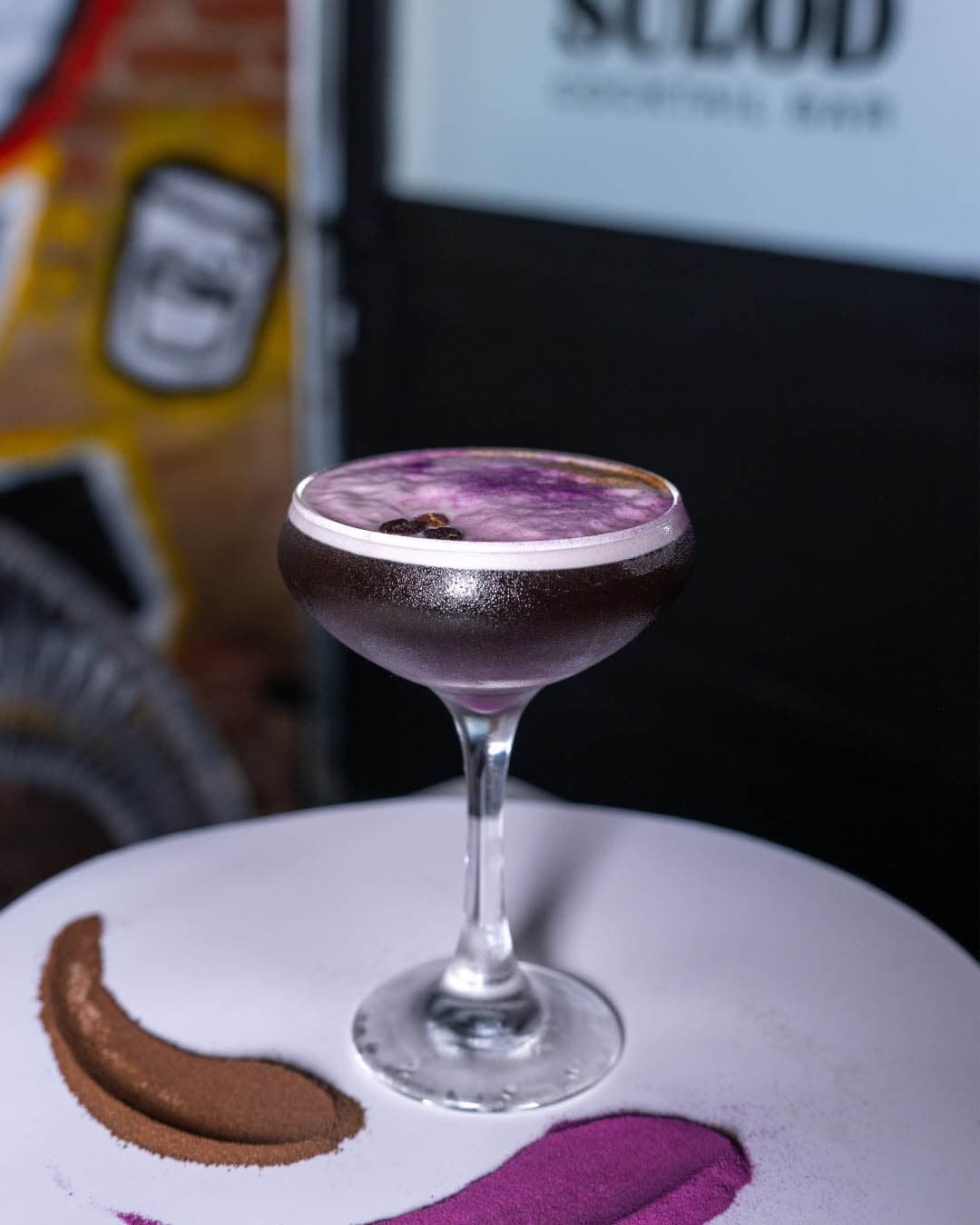 Purple Pick Me Up cocktail in a coupe glass on a smeared plate