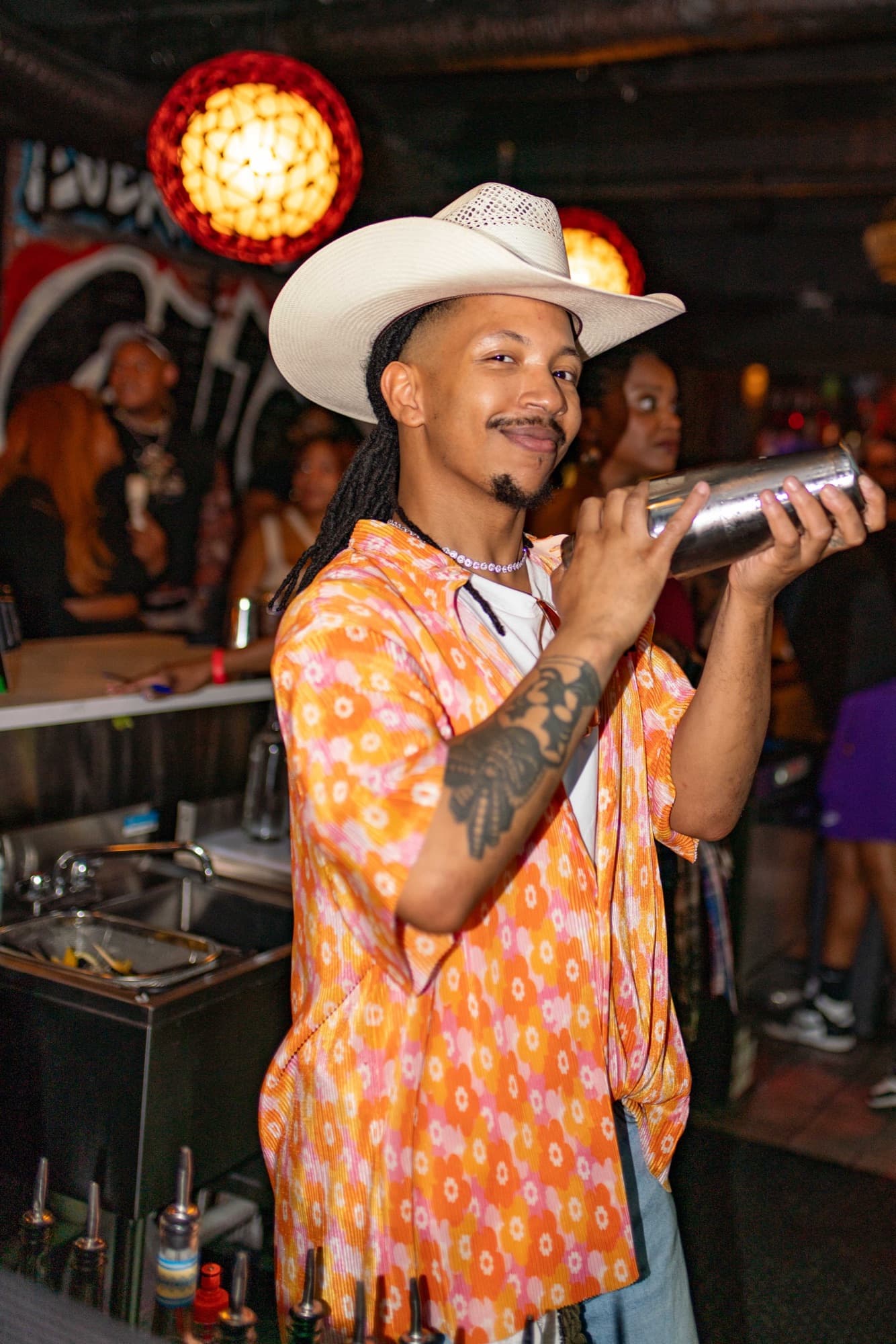 A guest bartender in a cowboy hat shaking a cocktail