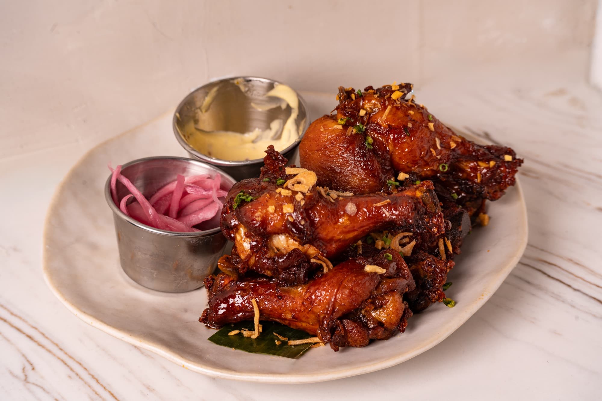 Lacquered Sulod Wings on a banana leaf with aioli and pickled onions